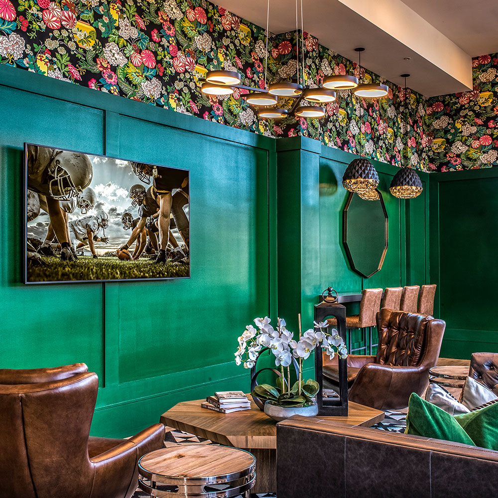 Leather soft seating in front of large TV displaying a football game in the residents' lounge at Halstead Salem